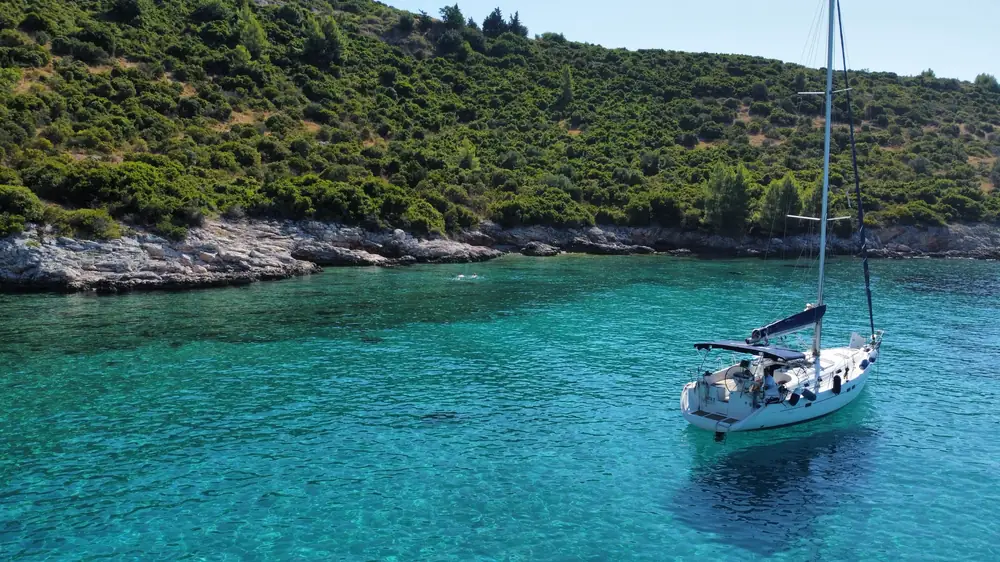 Sailing yacht anchored in a turquoise cove with a swimmer in the water
