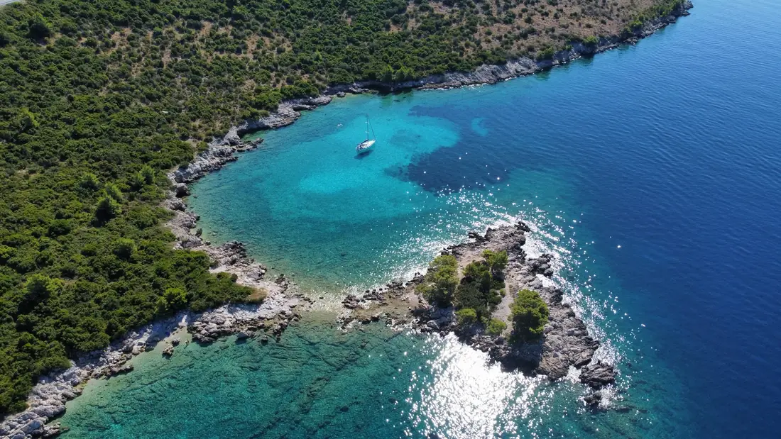 Aerial view of a quiet turquoise cove with a sailing yacht at anchor