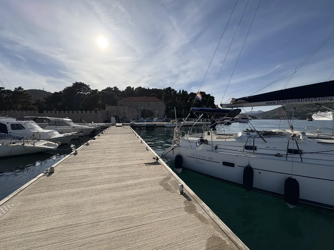 Our Beneteau Oceanis 411 moored at a pontoon, with a stone wall and pine trees on the shore