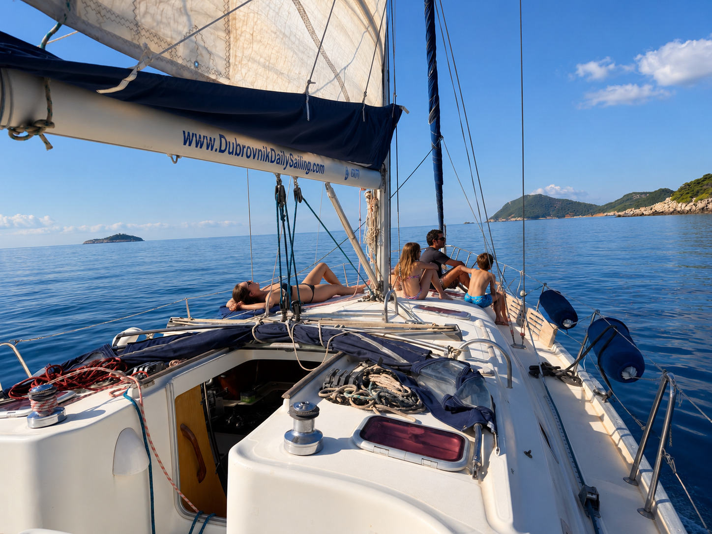 Guests relaxing on the foredeck of our sailing yacht under sail near Dubrovnik, with green islands on the horizon