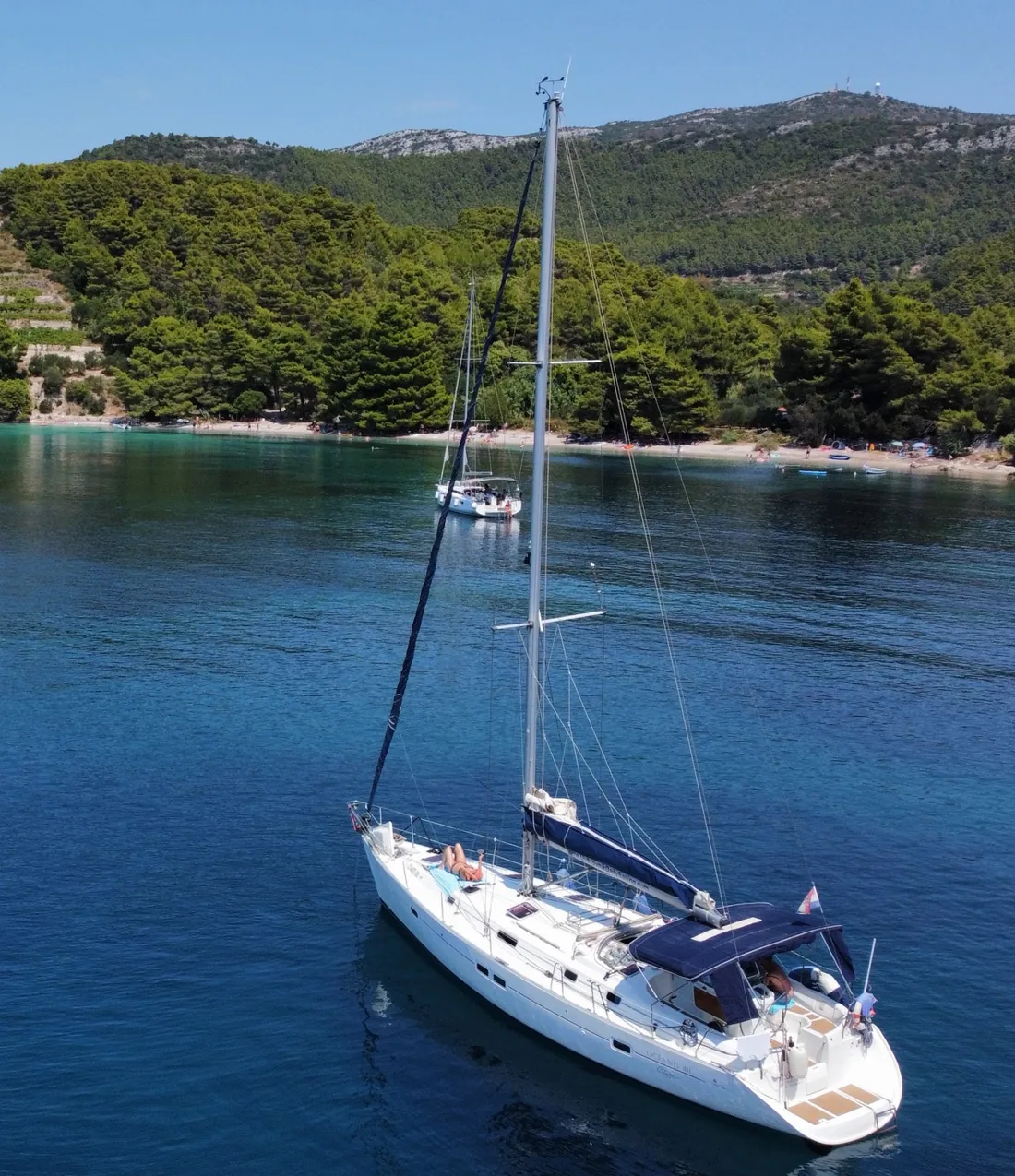 Our Beneteau Oceanis 411 at anchor in a calm bay, seen from the water with its full mast and rigging